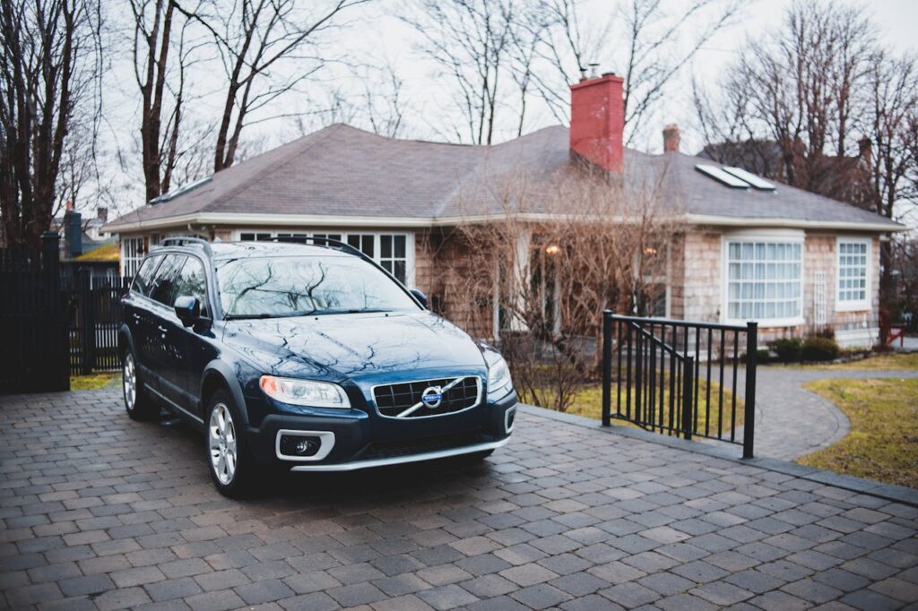 Exterior of new dark blue car placed near brick cottage surrounded by trees in cloudy day